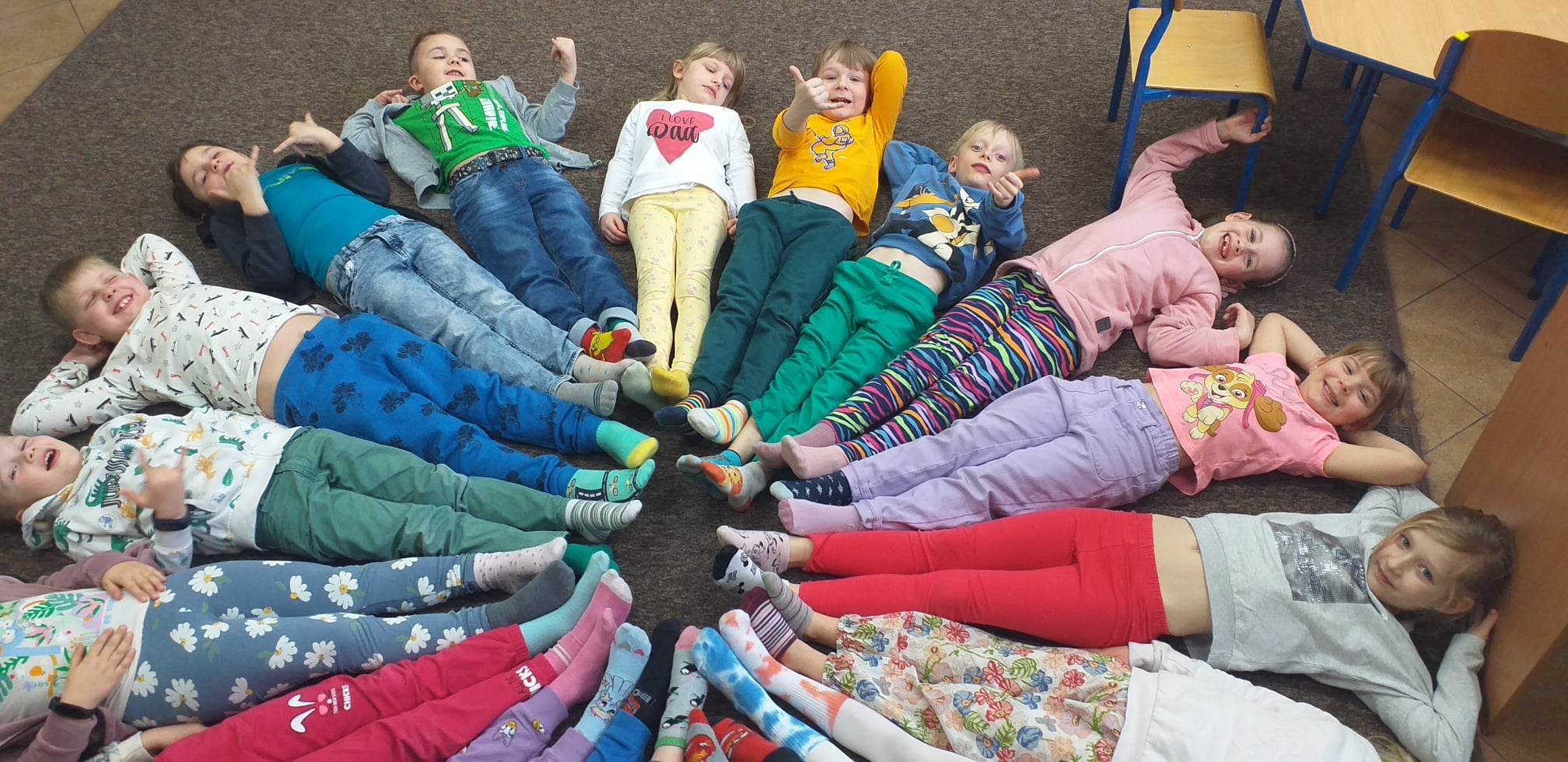 Dzieci leżące na podłodze stykające się na środku nogrami. Na nogach mają kolorowe, różne skarpetki