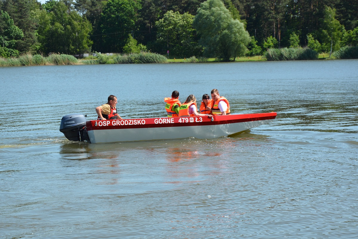 pięcioro ludzi w pomarańczowych kapokach pływają czerwono biała motorówka po zalewie 