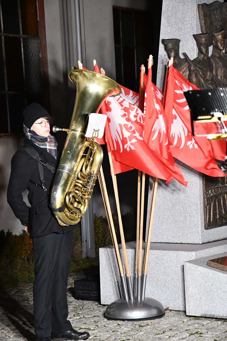 Muzyk z tubą przy flagach Powstańczych i pomniku.