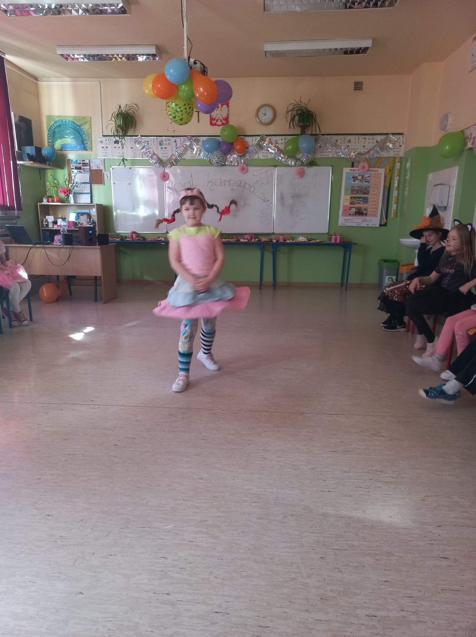 Dziewczynka z warkoczykami i różową sukienką na środku sali