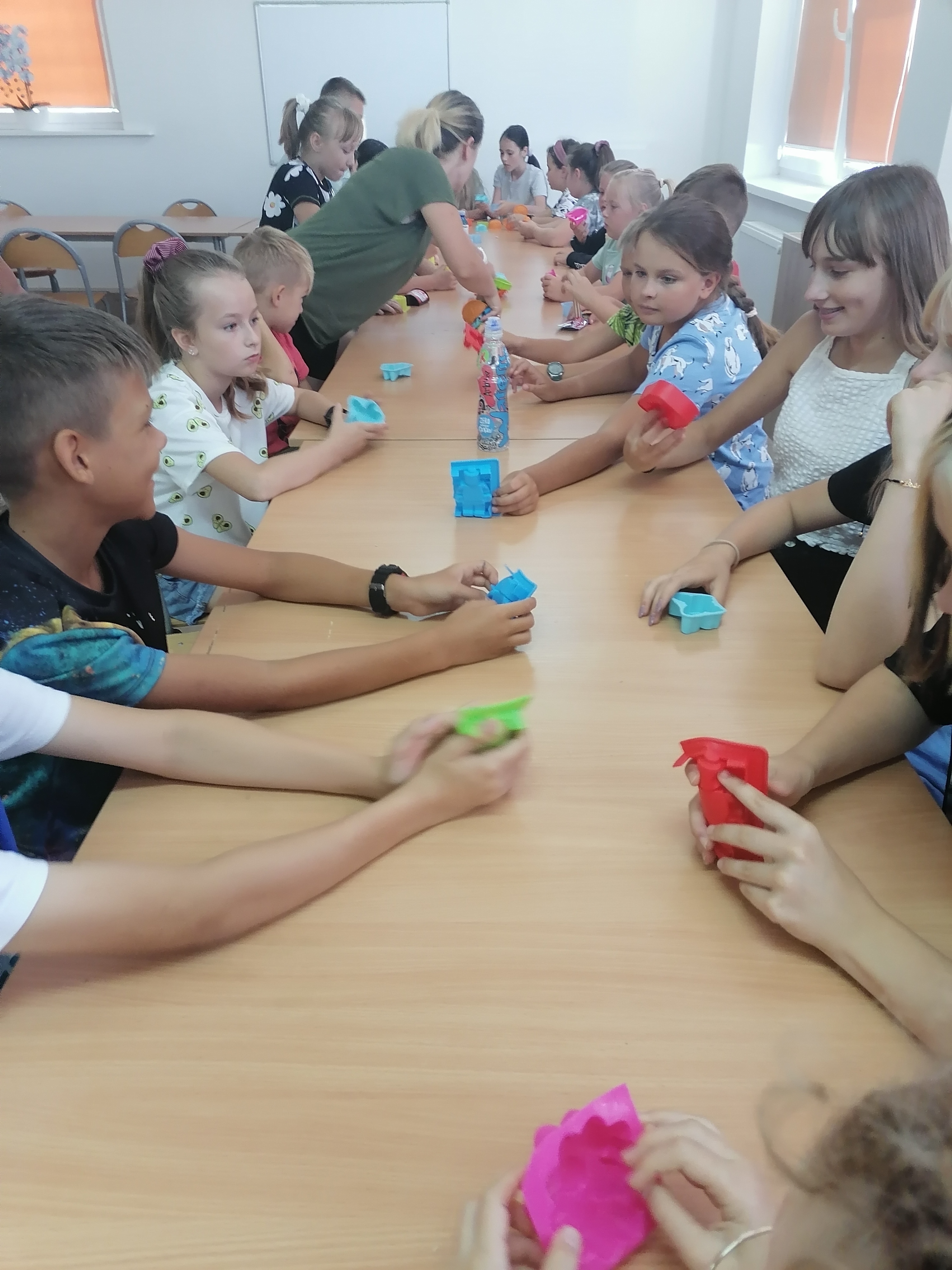 Zdjęcie przedstawia grupę dzieci wybierających kształty i rzeczy potrzebne do utworzenia mydełka glicerynowego.