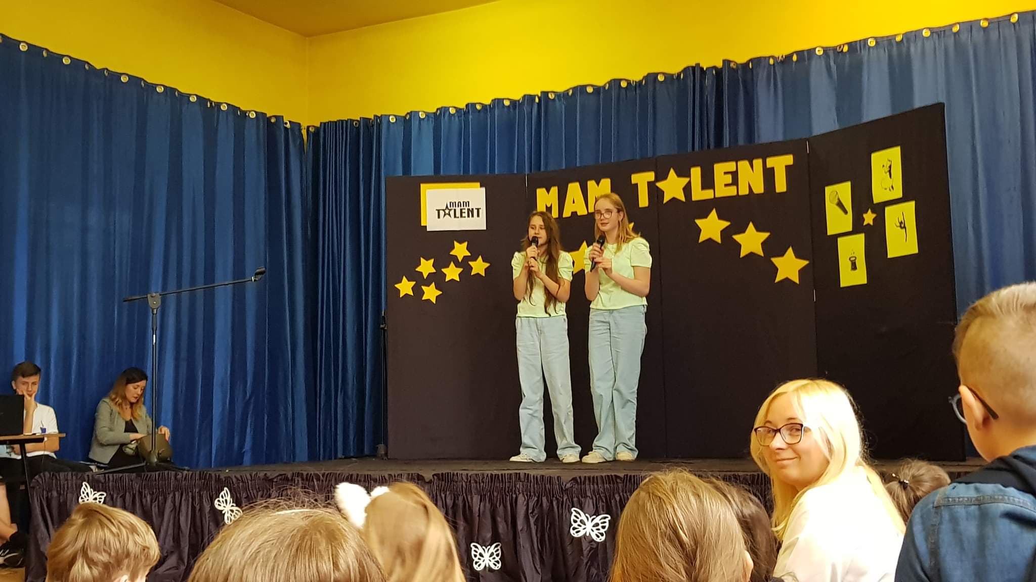 dwie dziewczynki na scenie śpiewają do mikrofonów trzymanych w rękach