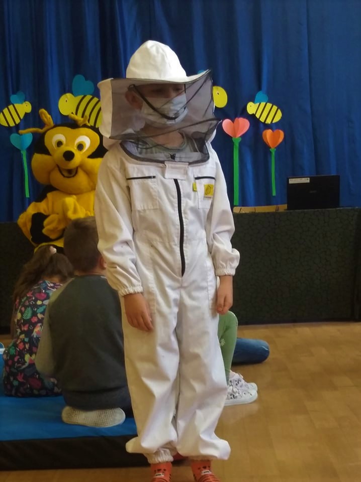 Dziecko ubrane w biały ochronny strój pszczelarza z kapeluszem i siatką wokół głowy