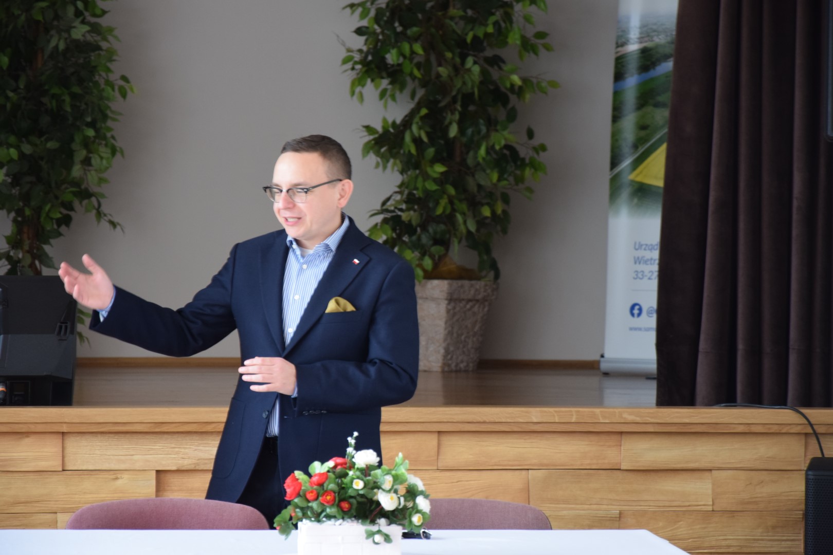 zdjęcie przedstawia Posła na Sejm RP Piotra Saka stojącego za stołem i wygłaszającego krótkie przemówienie