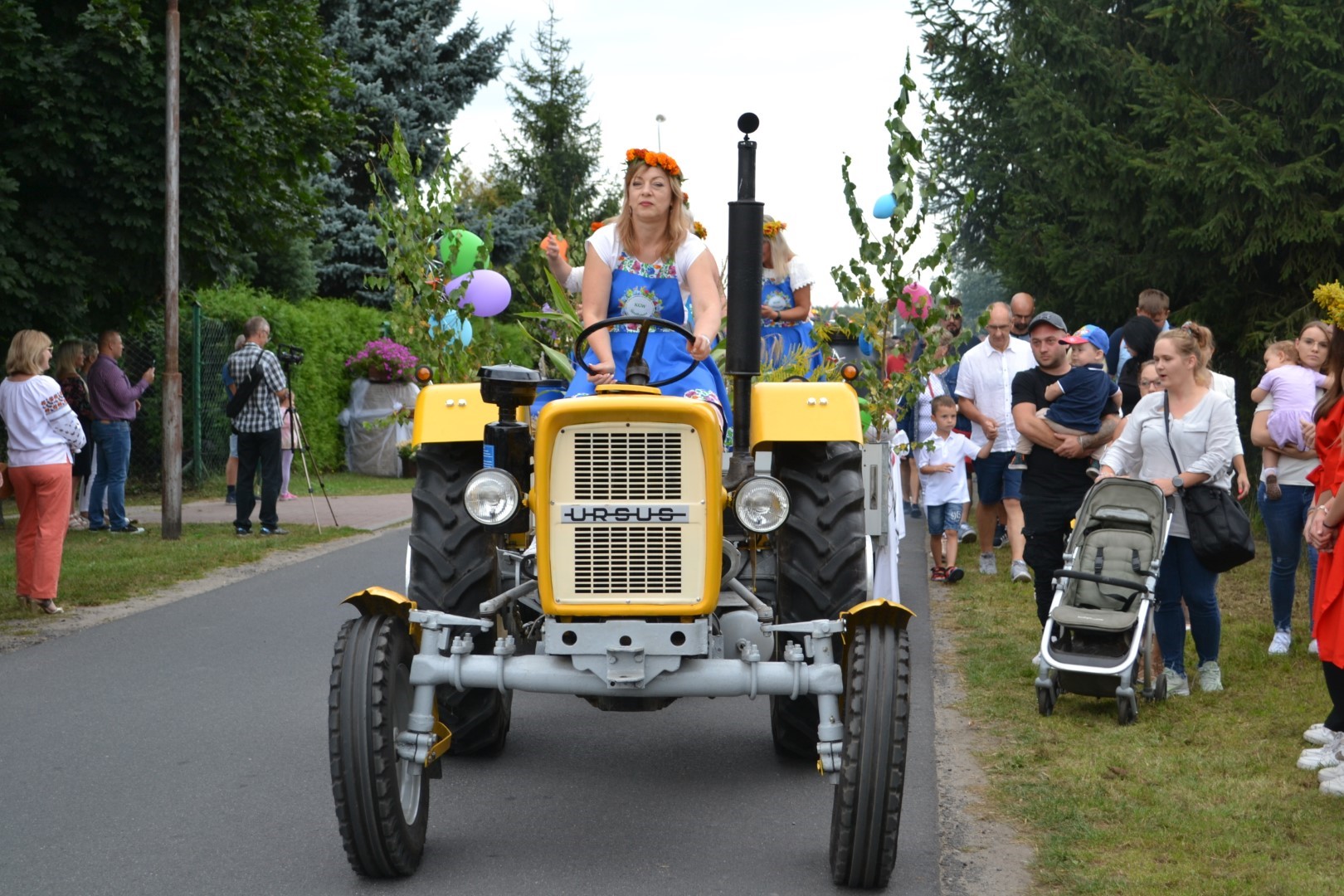 Na zdjęciu widać ludzi na poboczu i kobietę jadącą traktorem