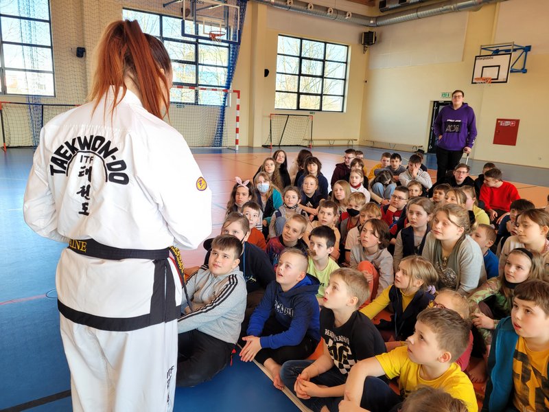 Zdjęcia, uczniowie na sali gimnastycznej z wraz z trenerką taekwondo