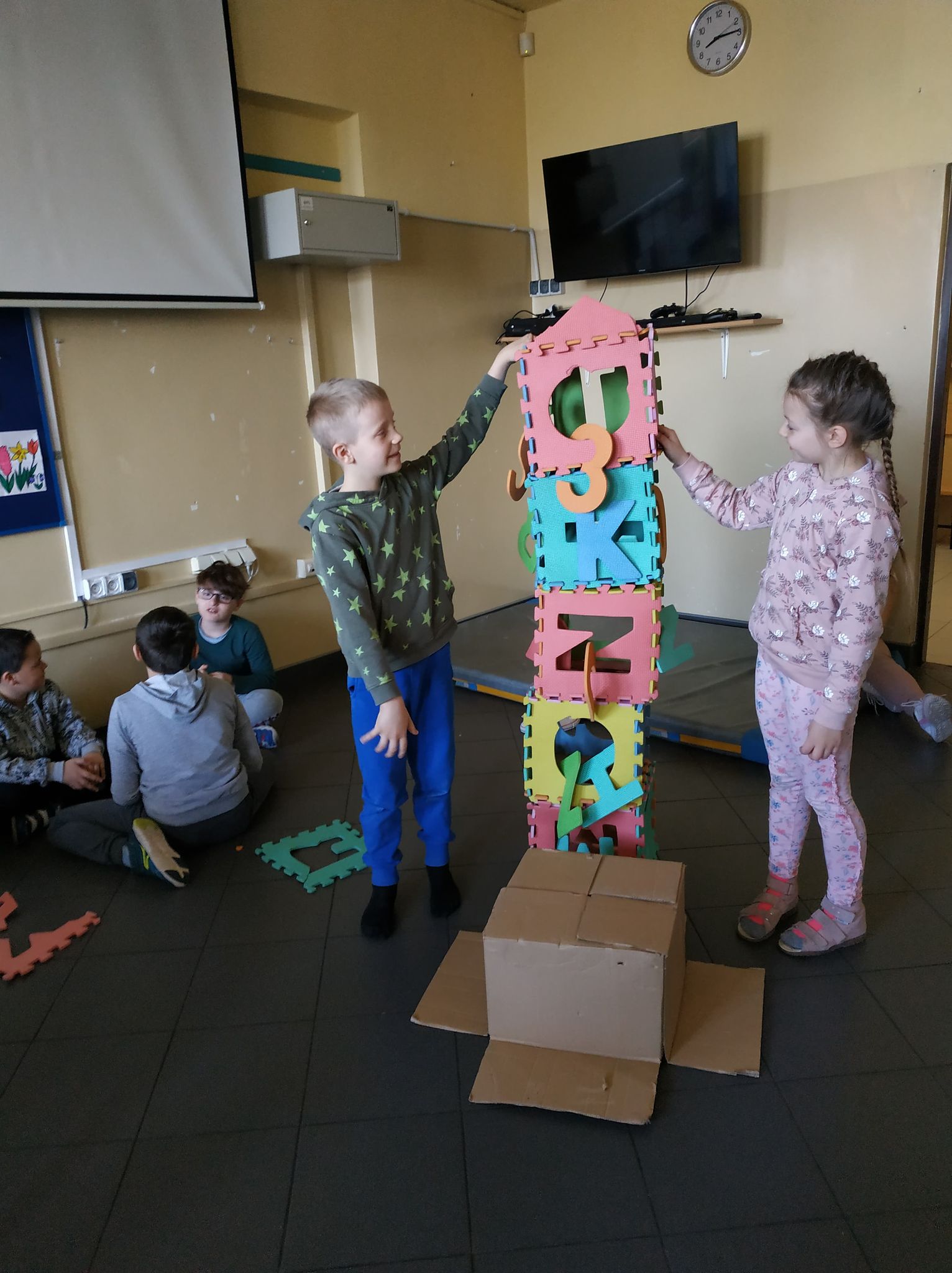 Wieża z kolorowych kartonów. Podtrzymują ją z obu stron dzieci
