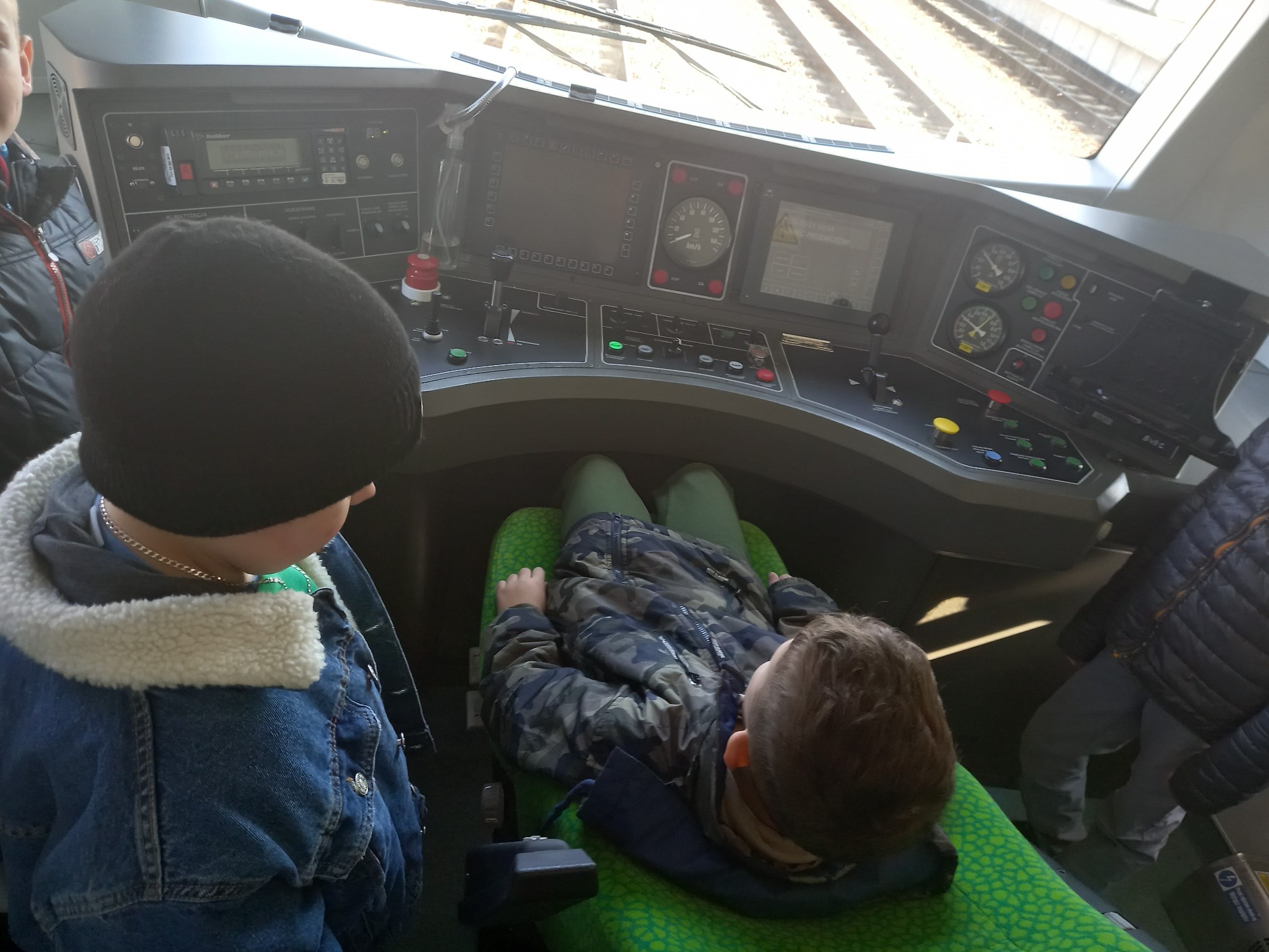 Dwoje chłopców siedzi w kabinie maszynisty. przed nimi konsola z guzikami i wskaźnikami