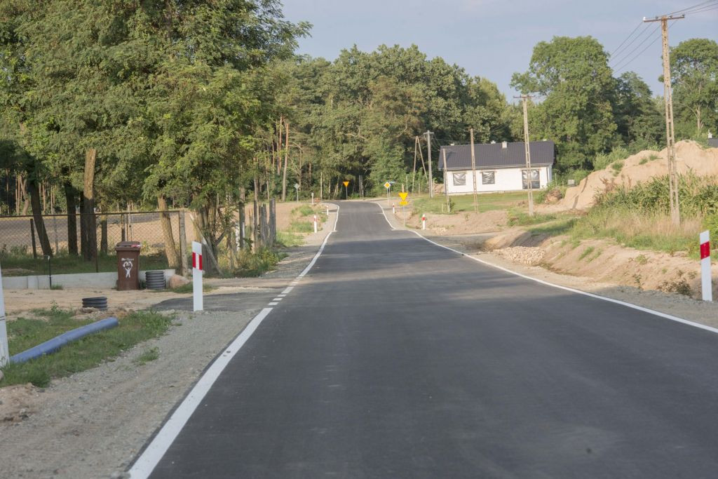 asfaltowa droga gminna w Klotyldzinie, po lewej fragment ogrodzenia i zjazd na posesję, po prawej napowietrzna linia energetyczna, w oddali dom mieszkalny