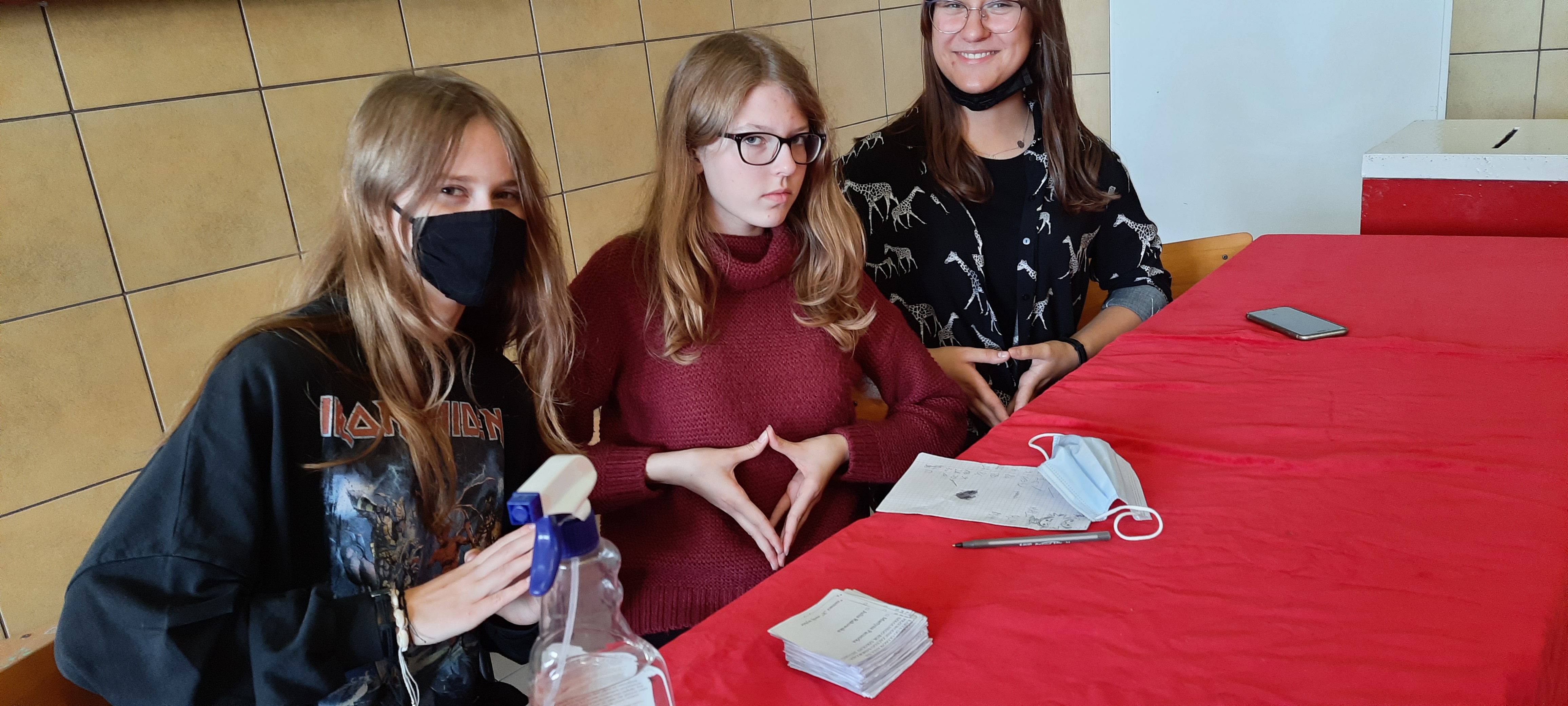 Trzy nastolatki siedzą przy czerwonym stole
