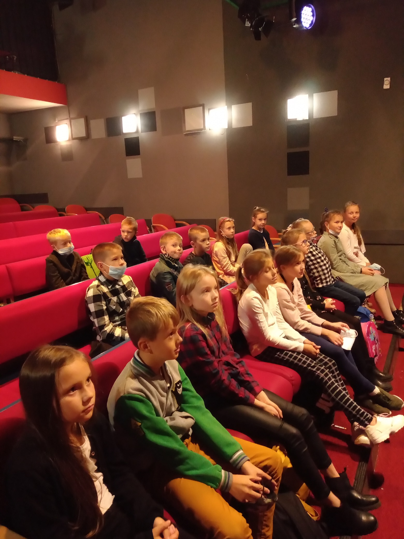 Dzieci siedzące na czerwonych fotelach na widowni teatru
