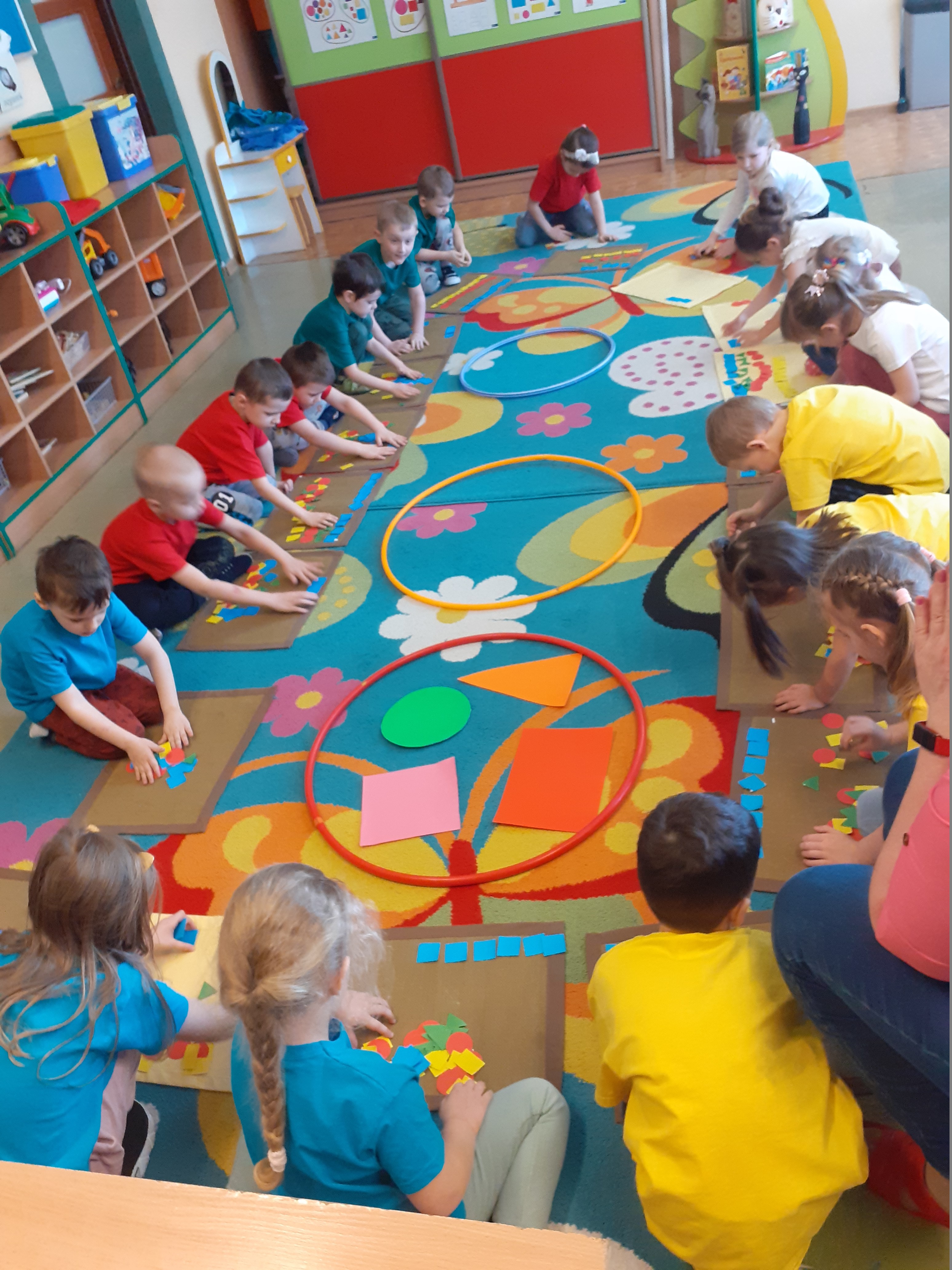 Dzieci siedzą na dywanie, układają figury w różnych kolorach 