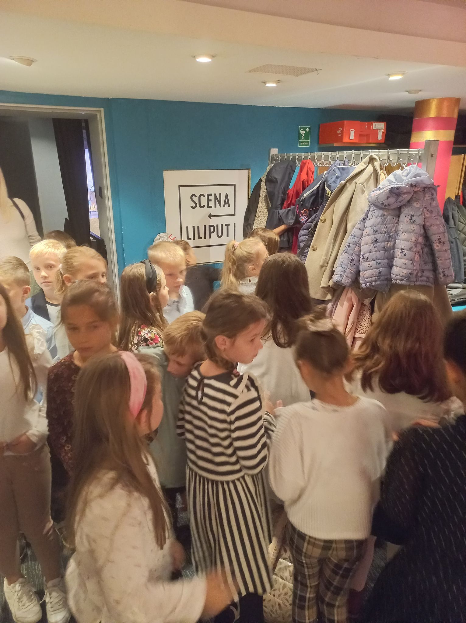 Dzieci stojący w pomieszczeniu z wieszakiem z kurtkami