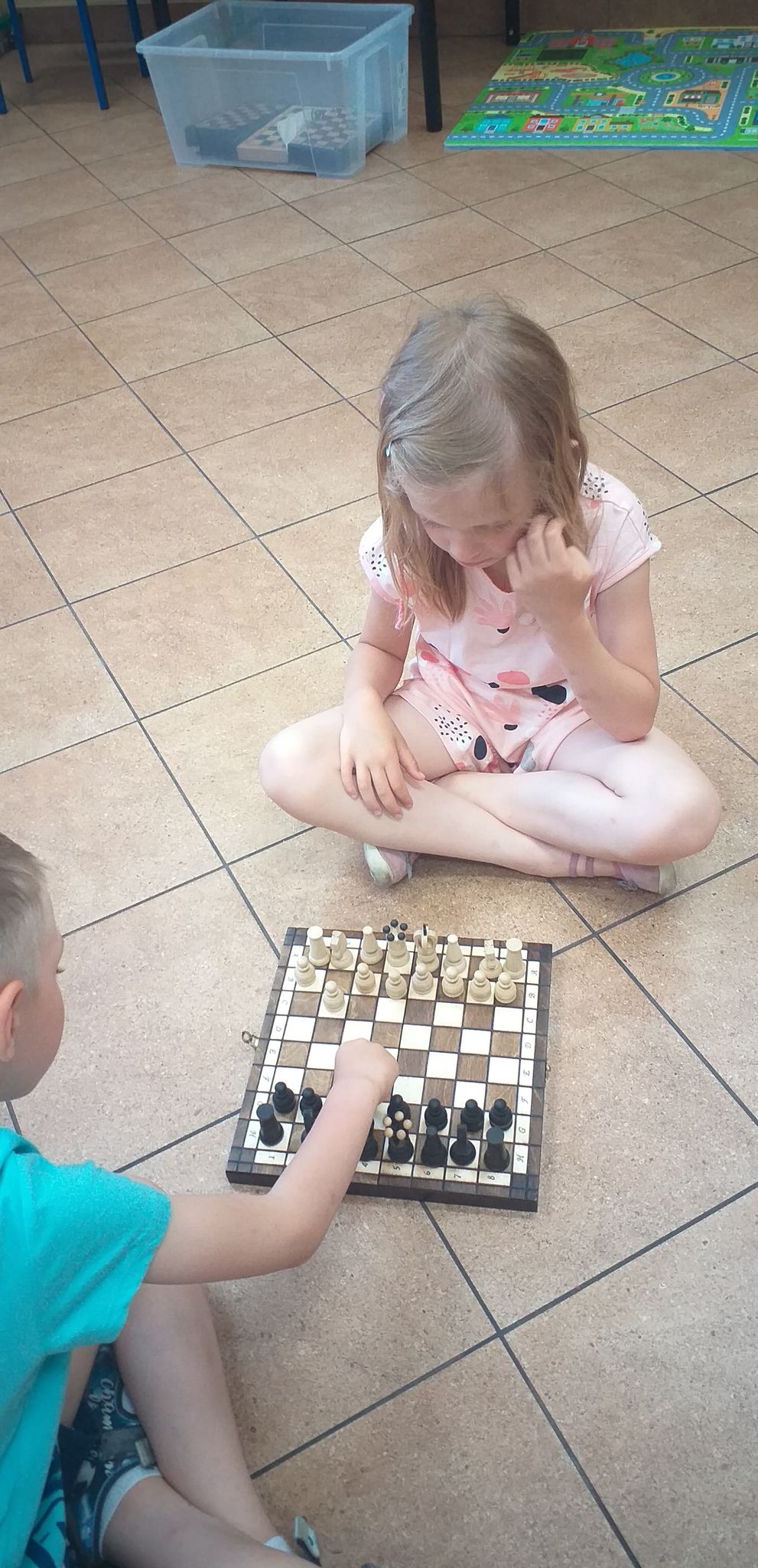 Dwoje dzieci gra w szachy na podłodze