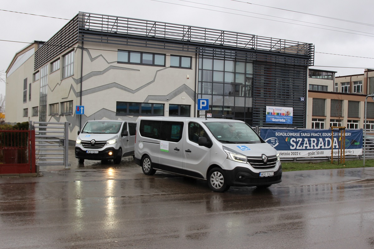 Na zdjęciu widać dwa szare samochody dostawcze załadowane pomocą humanitarną Powiatu Sokołowskiego. W tle gmach Hali Sportowej przy Zespole Szkół Nr 1 w Sokołowie Podlaskim.