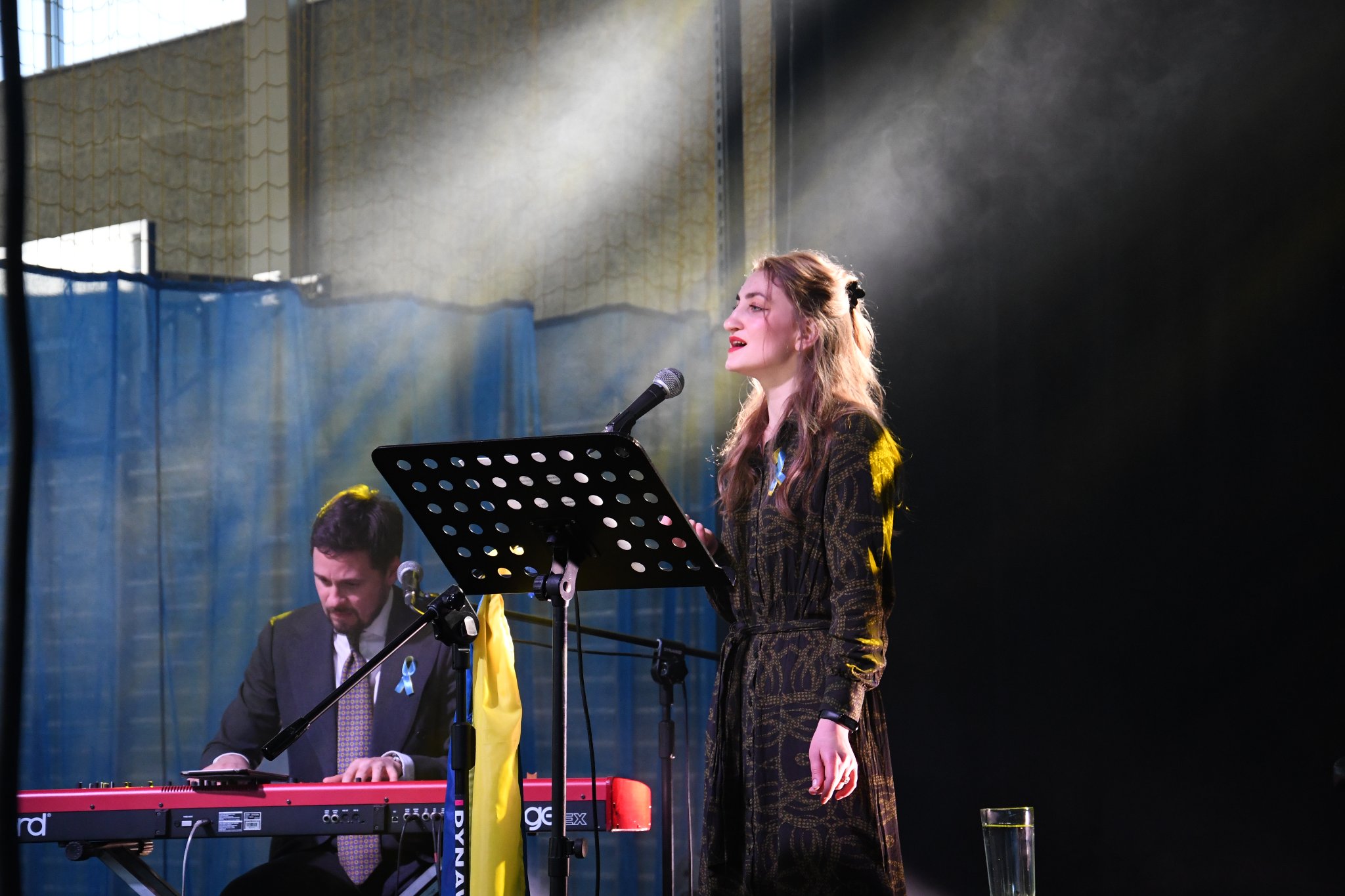 Na scenie widoczne są dwie osoby - wokalistka stojąca przy mikrofonie i po lewej stronie pianista. Wokalistka podczas robienia zdjęcia wykonywała utwór ukraiński.