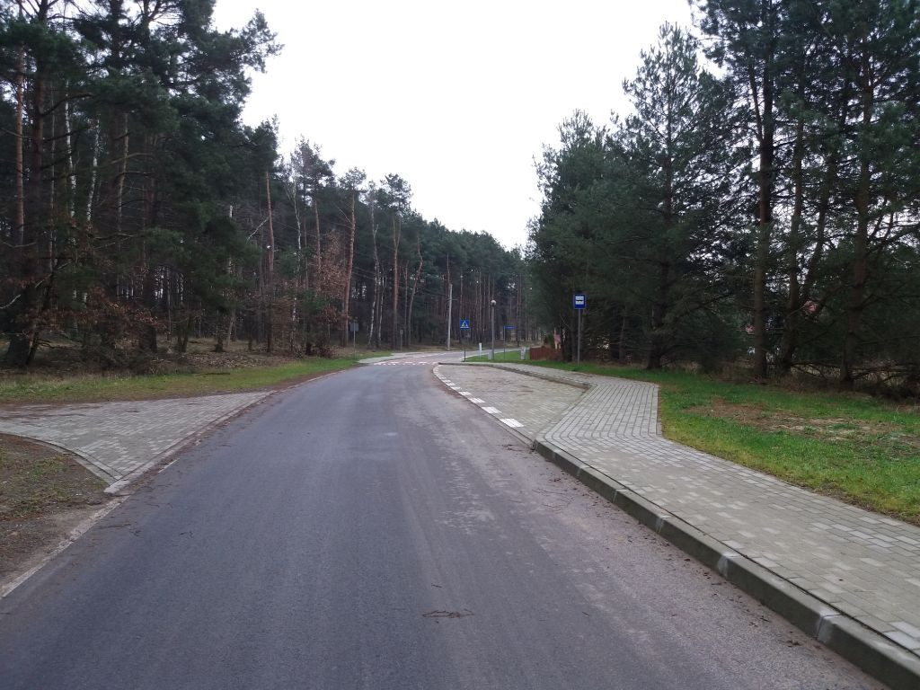 asfaltowa droga gminna nr 198015P Rutki-Klotyldzin, po lewej las i zjazd wykonany z kostki brukowej, po prawej chodnik z kostki brukowej z zatoczką autobusową
