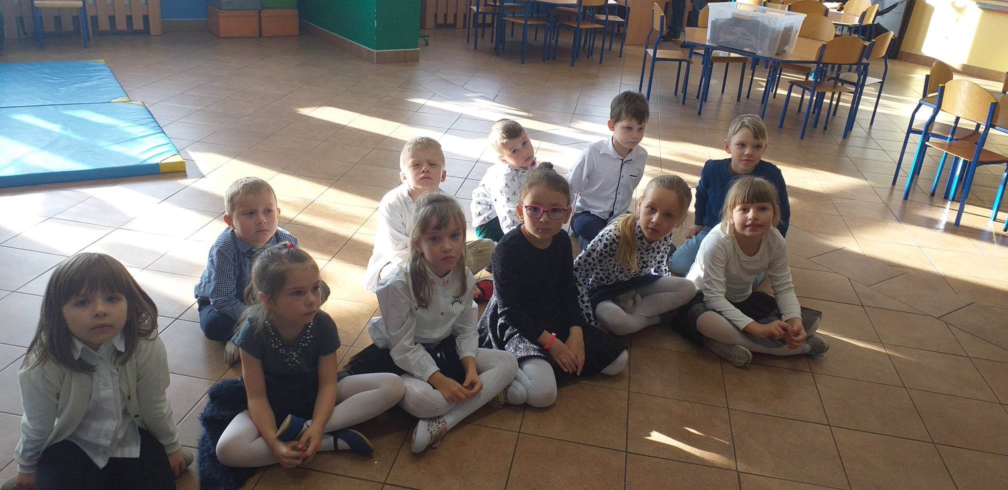 Dzieci siedzą na podłodze w dwóch rzędach