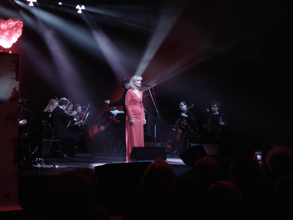 Wokalistka Katarzyna Żak śpiewa na scenie, za nią Sądecka Orkiestra Kameralna w składzie 10 osób z dyrygentem Leszkiem Mieczkowskim.