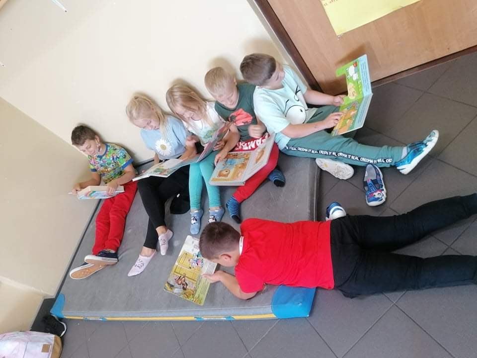 Dzieci siedzą na materacu i czytają książki