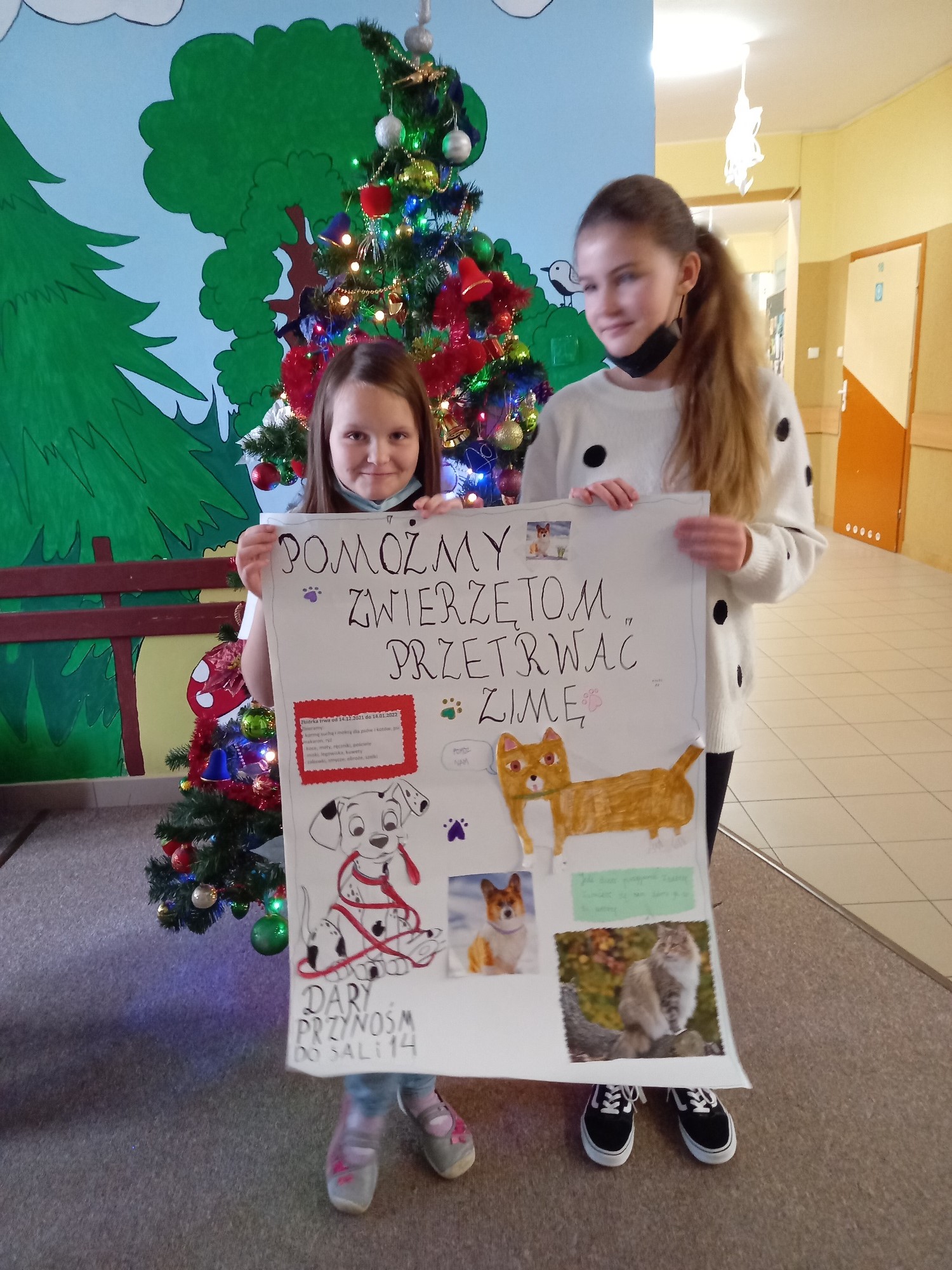 Dwie dziewczynki trzymają kartę ze zdjęciami psów i kotów oraz napisem Pomóżmy zwierzętom przetrwać zimę