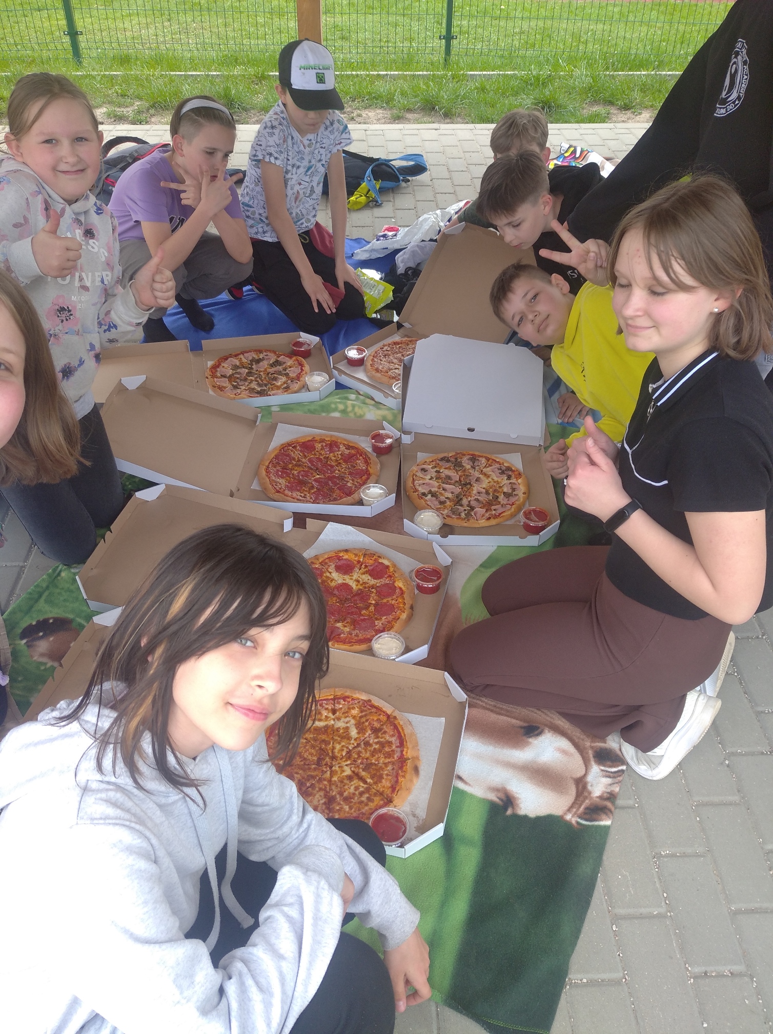 Dzieci jedzą pizzę ułożoną w kartonowych pudełkach przed nimi