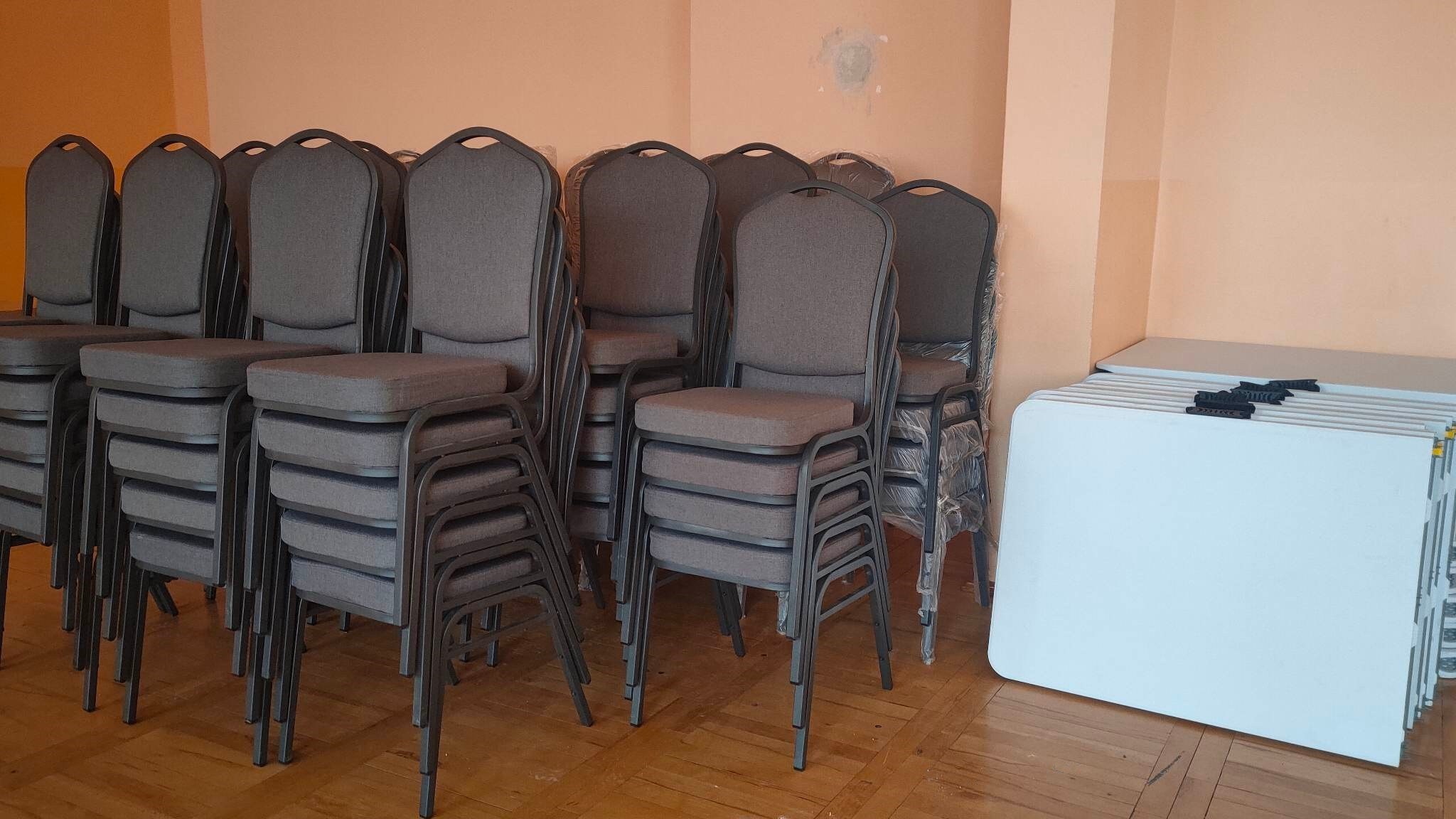 zdjęcie przedstawia szare krzesła bankietowe ustawione jedno na drugim w trzech rzędach pod ścianą