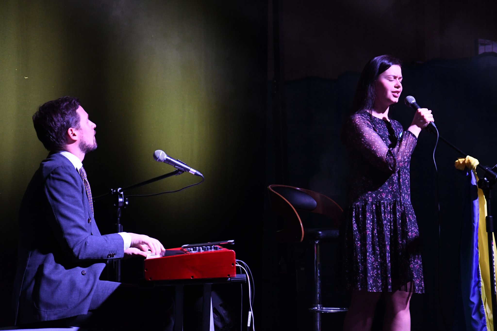 Na scenie widoczne są dwie osoby - wokalistka stojąca przy mikrofonie i po lewej stronie pianista. Wokalistka podczas robienia zdjęcia wykonywała utwór ukraiński. Zdjęcie zrobione z prawej strony.