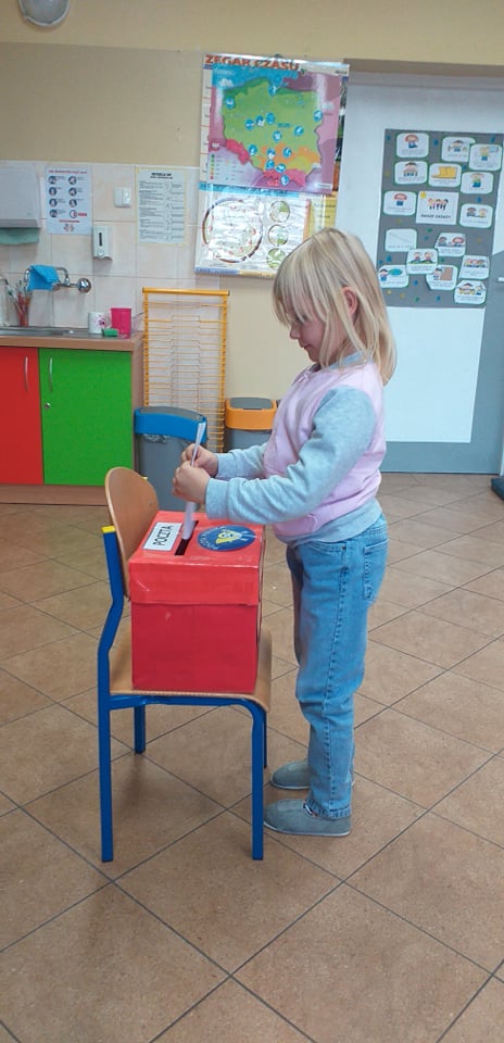 Dziewczynka wkłada kartkę do czerwonej skrzynki z napisem Poczta