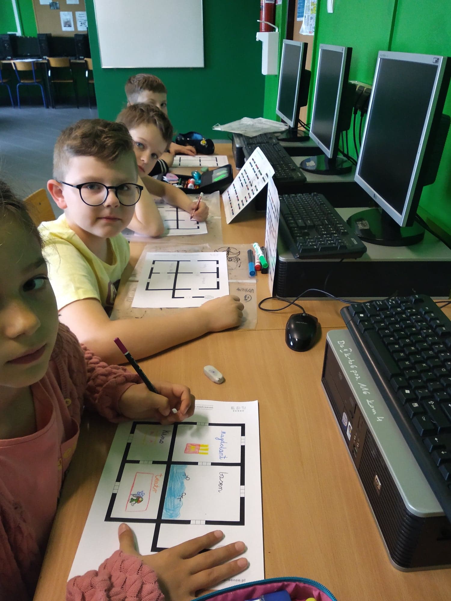 Dzieci siedzące przed komputerami wypełniają karty pracy