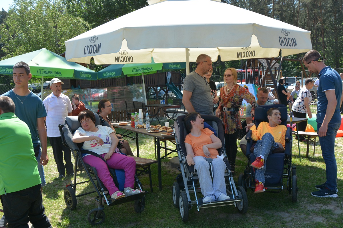 troje ludzi siedzi na specjalnych wózkach inwalidzkich wokół nich stoją ludzie 