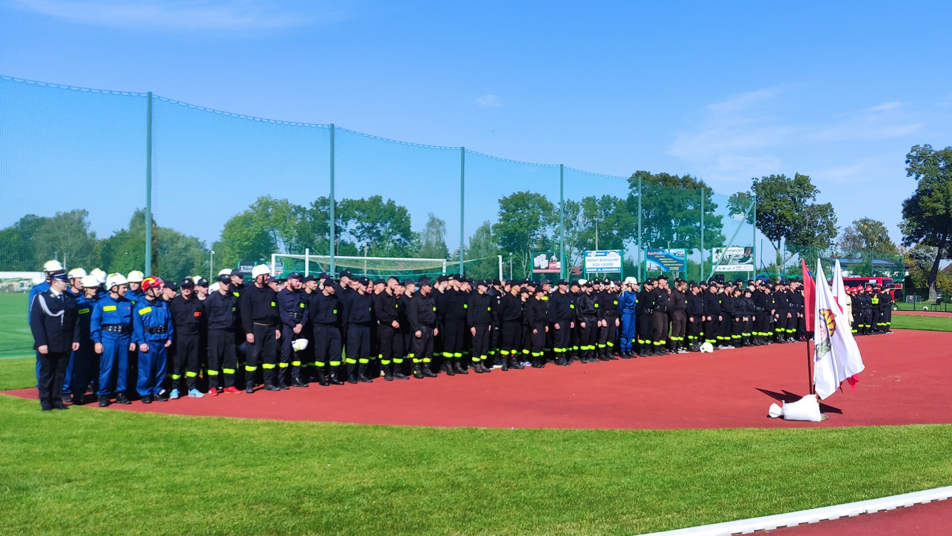 Zdjęcie grupowe wszystkich strażaków poszczególnych drużyn w mundurach bojowych. Uczestnicy stoją w szeregu. W tle płyta boiska stadionu miejskiego w Sokołowie Podlaskim