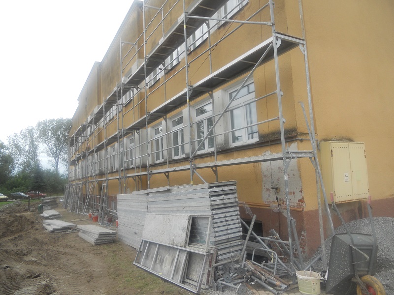 Zdjęcie przedstawia boczne ujecie przedniej części budynku Szkoły podstawowej w Wietrzychowicach w trakcie prac termomodernizacyjnych.
