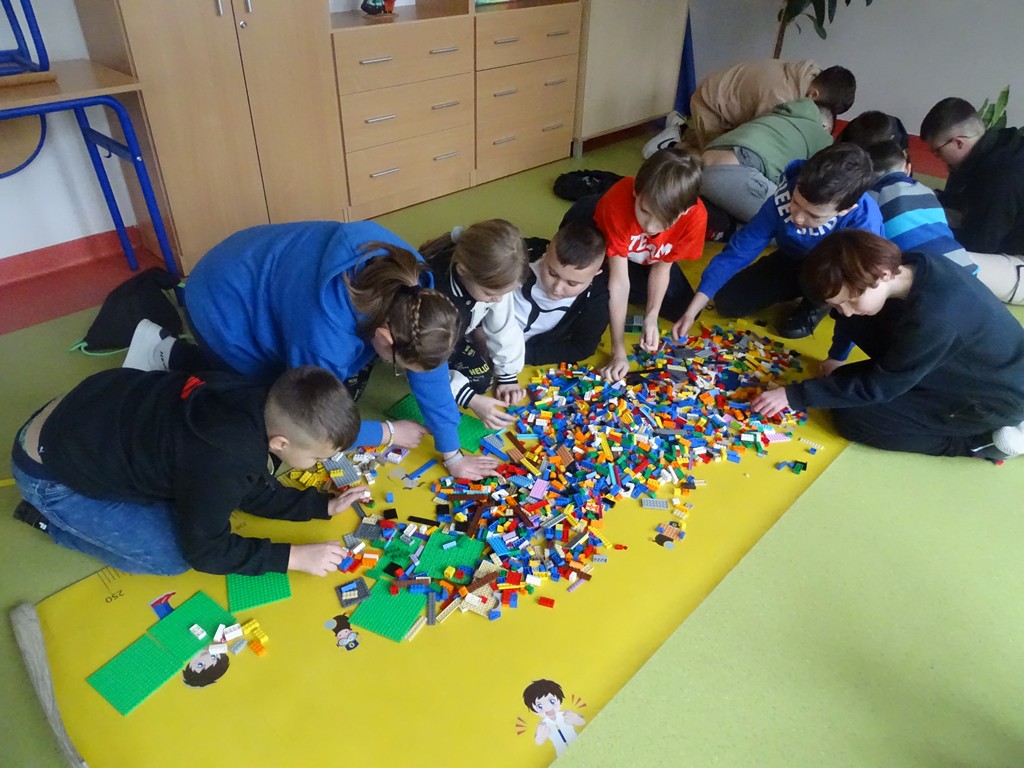 Zdjęcie przedstawia grupkę dzieci, które dostały za zadanie zbudowanie domku z otrzymanych klocków LEGO