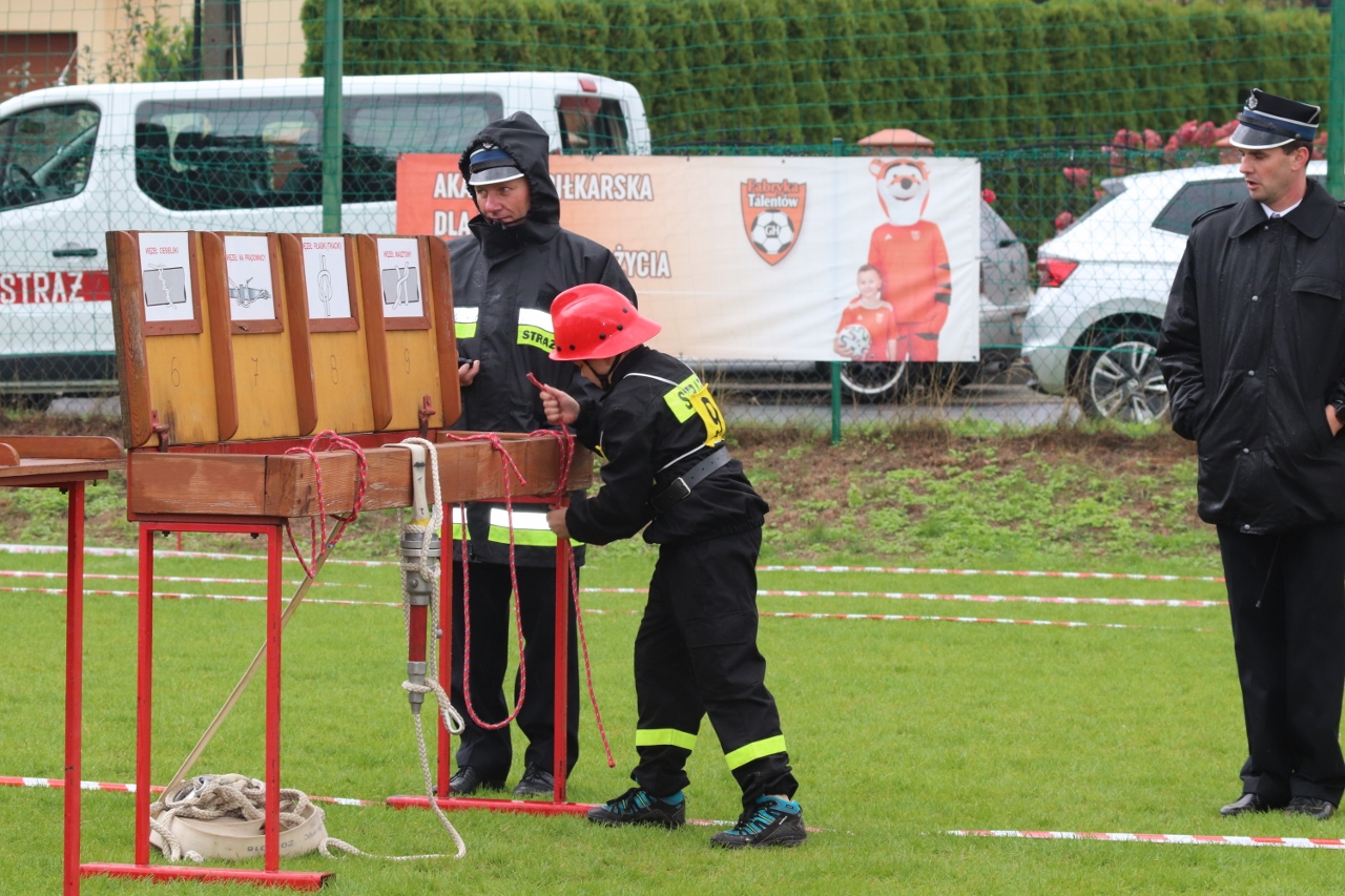 Chłopiec w stroju strażaka bierze udział w konkurencji podczas zawodów strażackich 