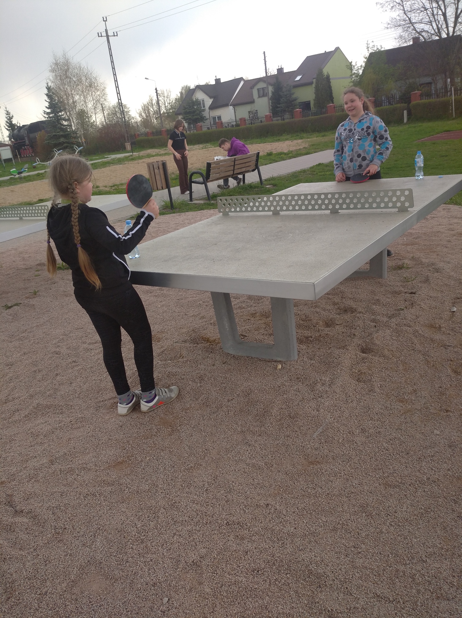 Dwie dziewczynki grają na betonowym stole do ping ponga na dworze