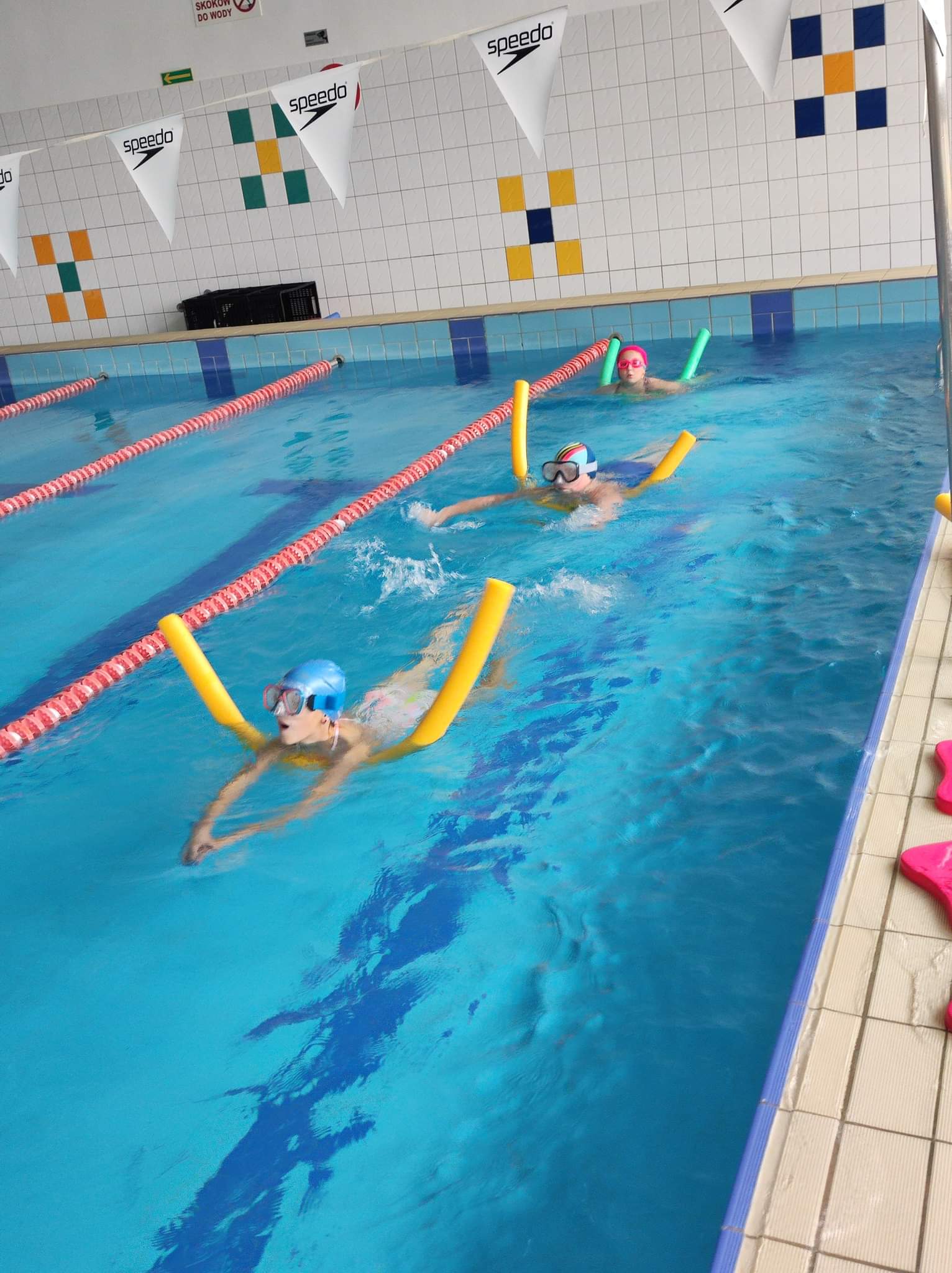 zdjęcie prezentuje troje dzieci w basenie uczących się pływać