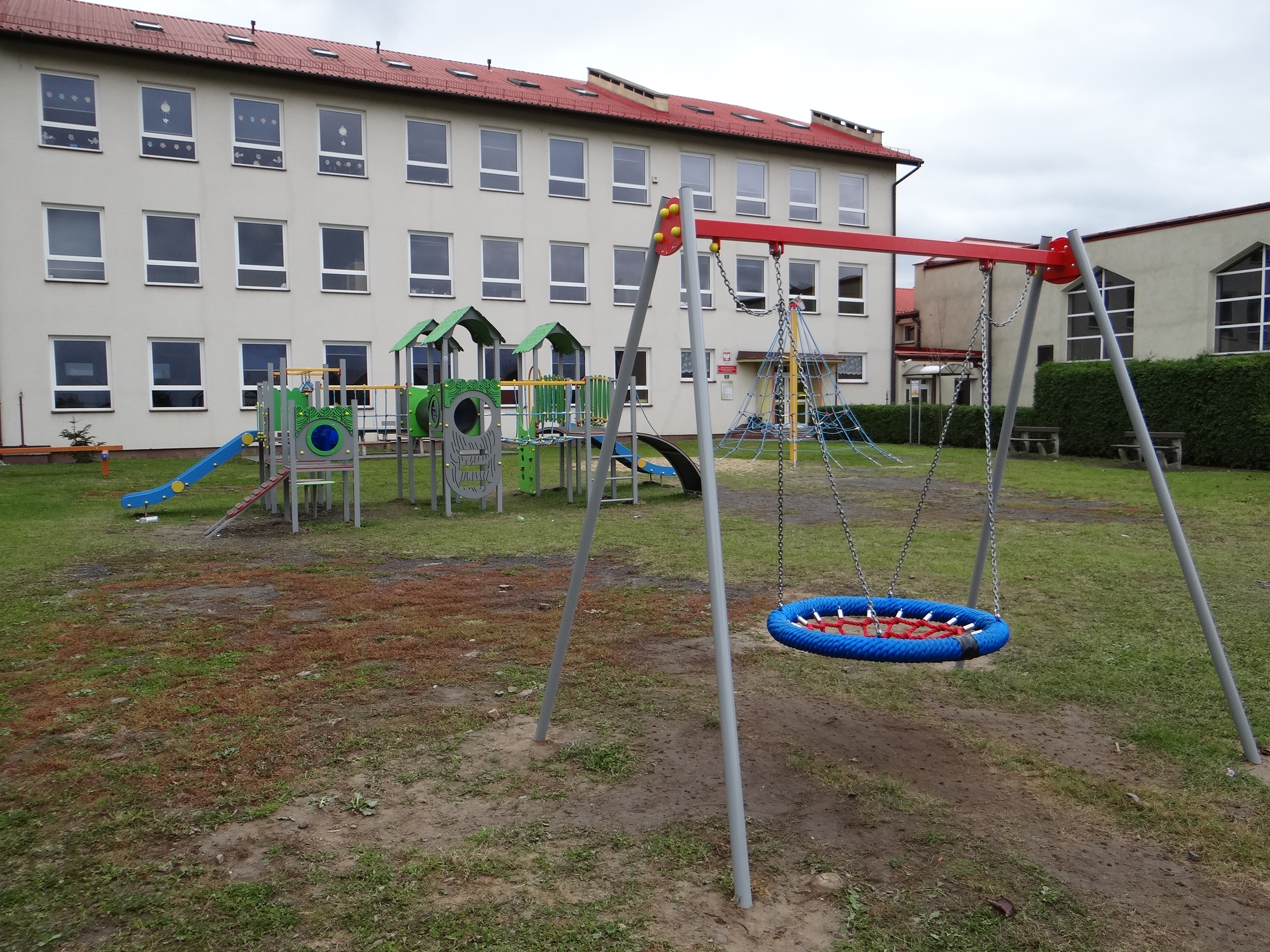 Ogólnodostępny plac zabaw przy Szkole Podstawowej w Pogwizdowie po modernizacji (2). Widoczna część urządzeń placu. Z tyłu budynek szkolny (skrzydło wschodnie) i hala sportowa.