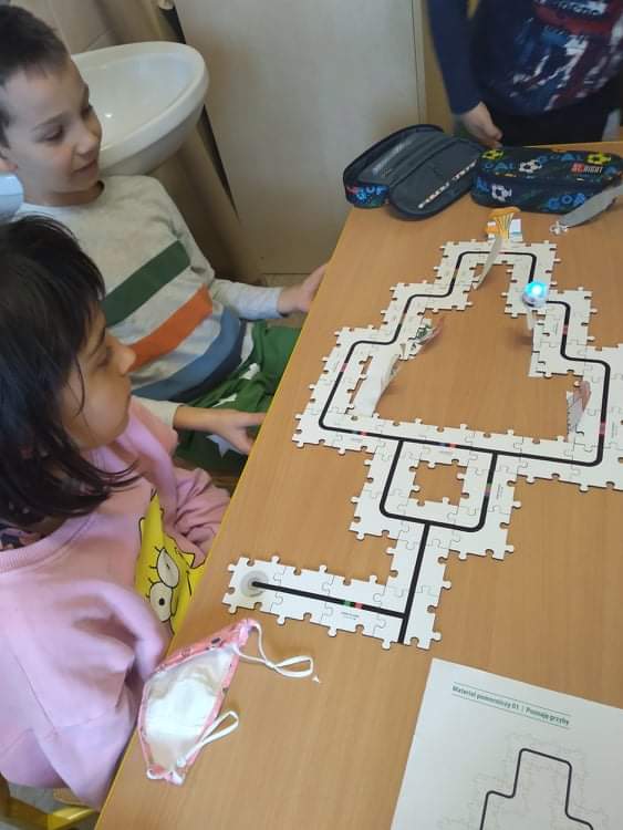 Dzieci siedzą przy stoliku. Na stole rozłożone puzzle.