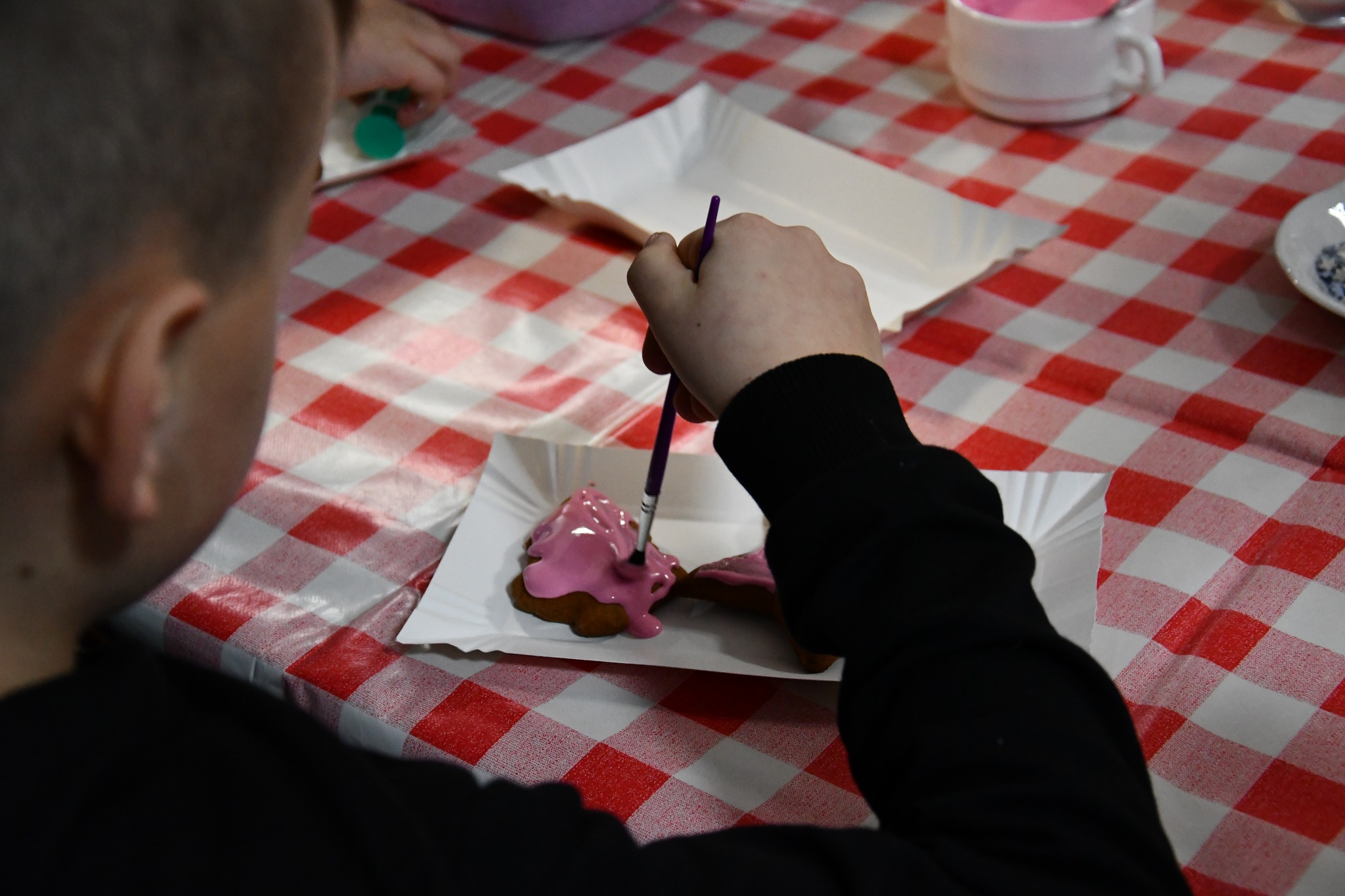 Chłopiec maluje różowym lukrem piernik w kształcie choinki.