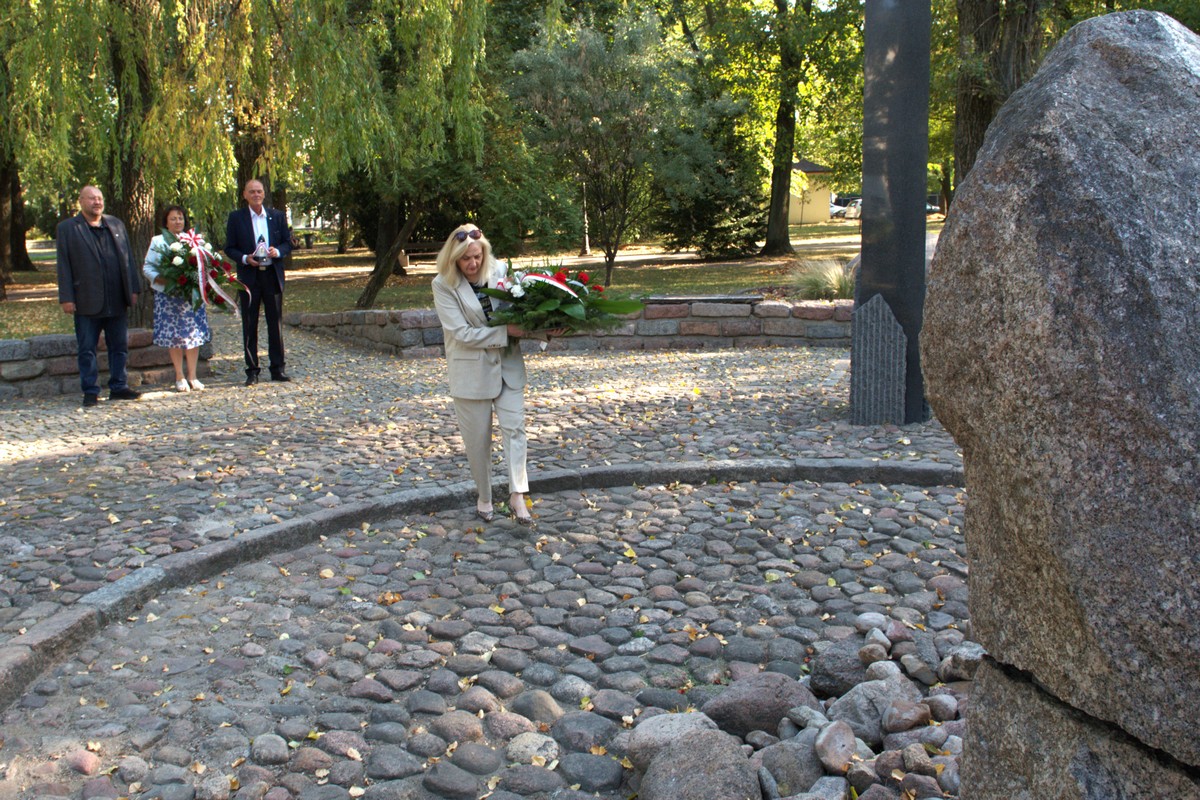 Na zdjęciu widać dyrektor biura senatora RP Waldemara Kraski, która zmierza w kierunku centralnej części pomnika Czynu Niepodległościowego, który stanowi przecięty poprzecznie na pół kamień z napisem Bóg, Honor, Ojczyzna. W tle delegacja powiatu sokołowskiego.