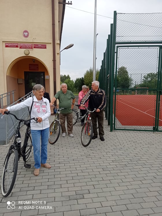 Seniorzy przed budynkiem Klubu Seniora z rowerami wybierają się na wycieczkę