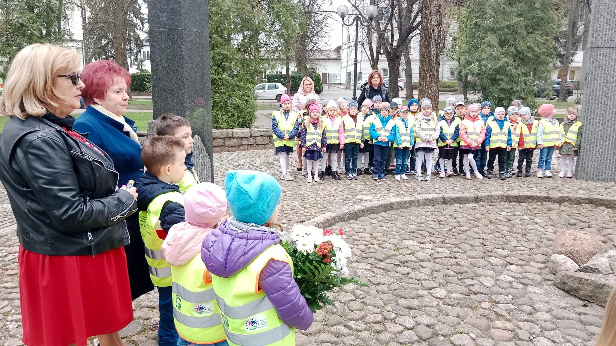 Nauczyciele i dzieci przy pomniku Czynu Niepodległościowego