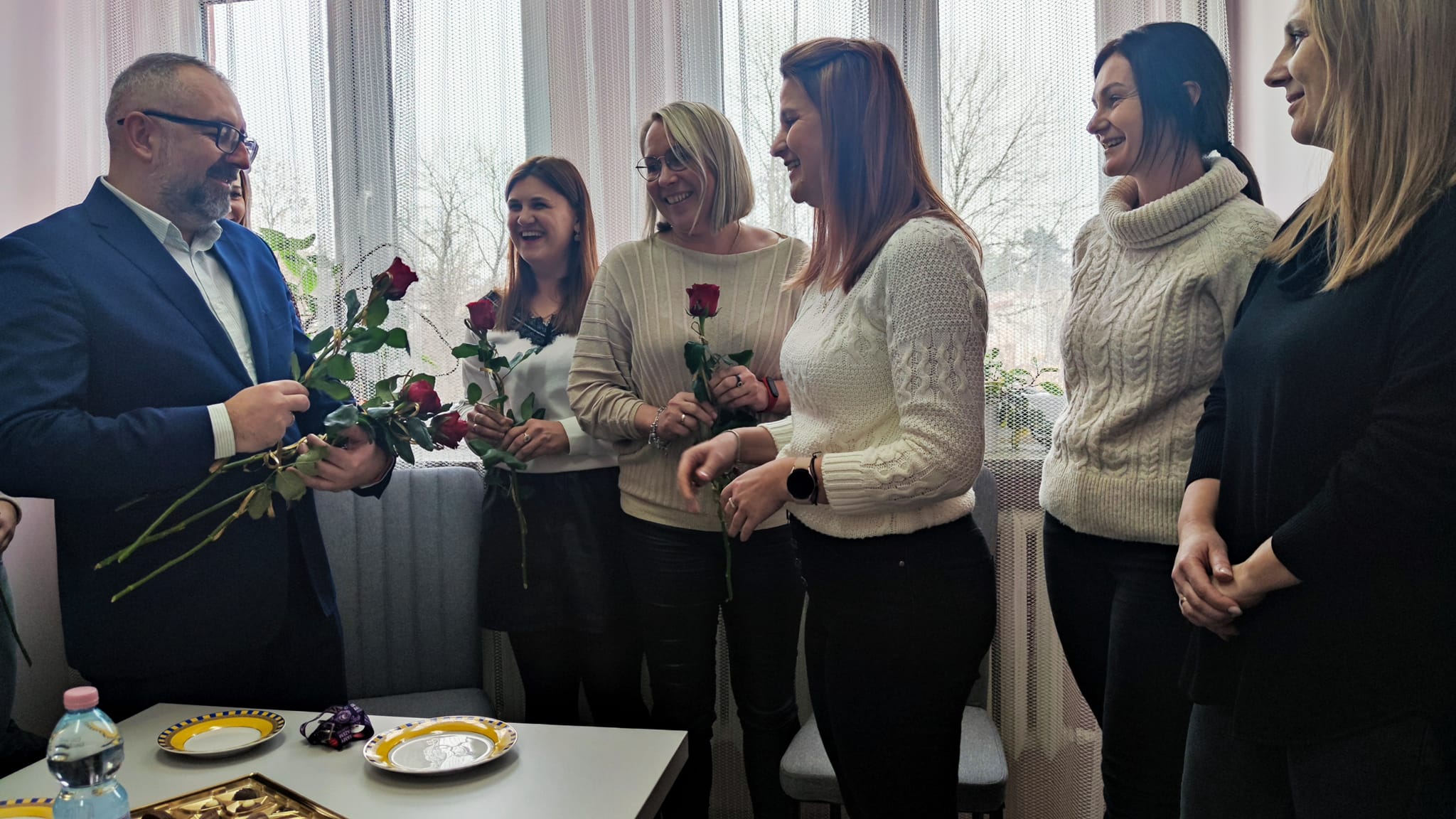 Zdjęcie przedstawia Starostę Krzysztofa Bieńkowskiego wręczającego czerwone róże pracownicom socjalnych placówek podległych Powiatowi.