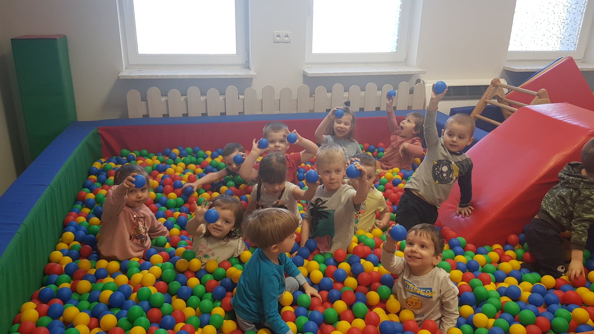 Dzieci bawią się w basenie z kolorowymi kółkami . Pokazują kulkę w kolorze niebieskim