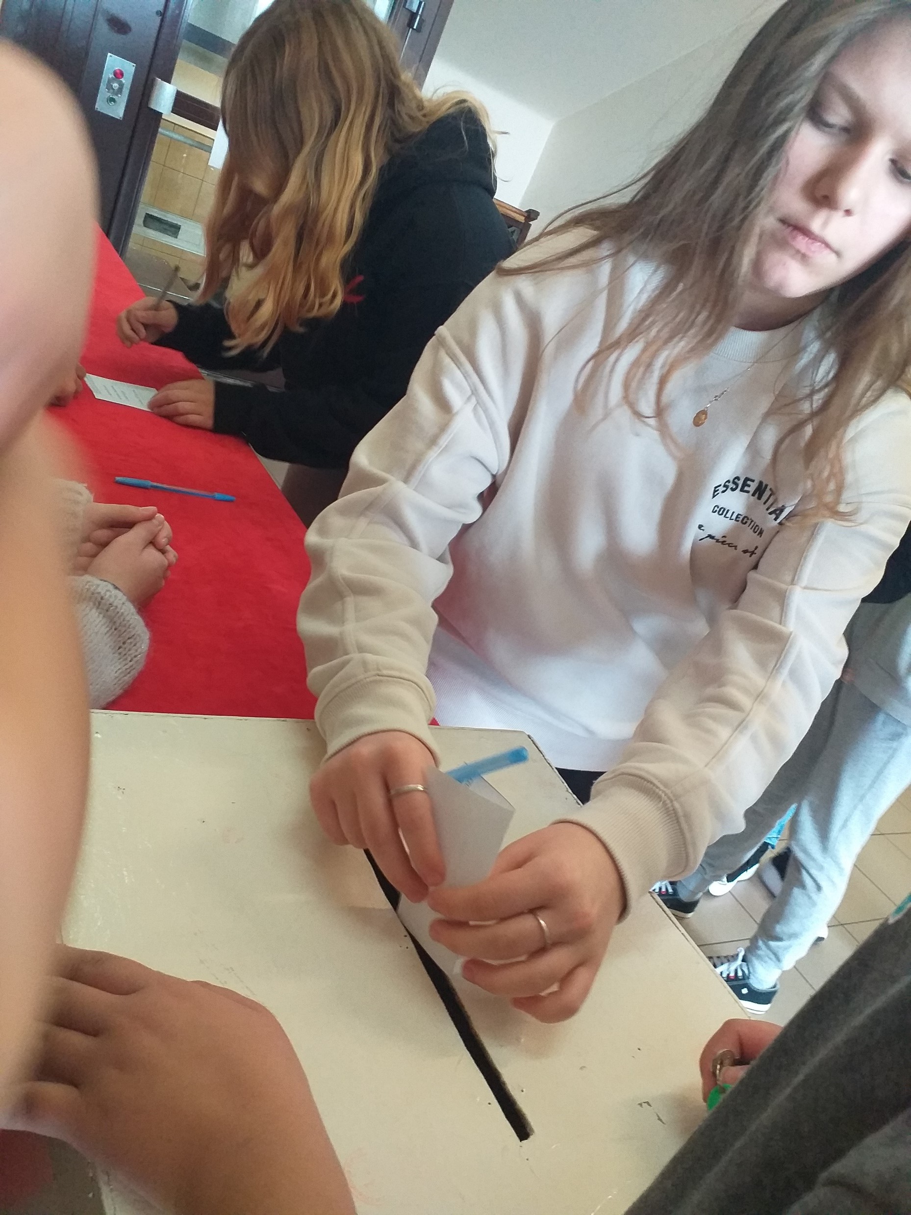 Dziewczynka w białej bluzie wkłada kartkę papieru przez wąską dziurę do urny