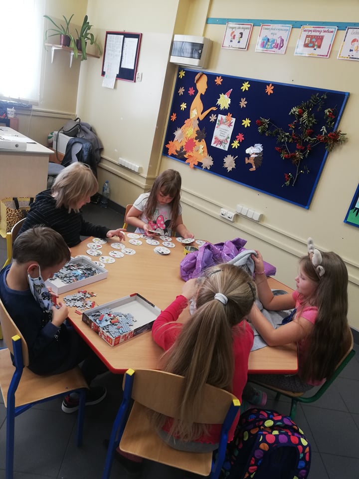 Dzieci siedzą przy stoliku i układają puzzle