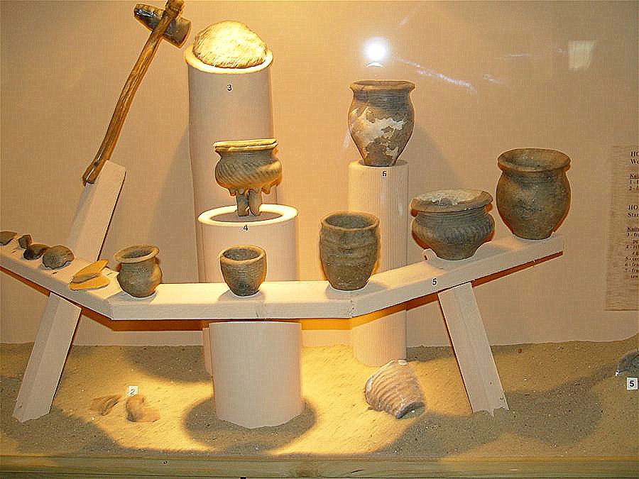 Na białych stojakach ustawione dzbanki, naczynia i różne przedmioty wydobyte przez archeologów na terenie gminy Grodzisko Dolne. 
