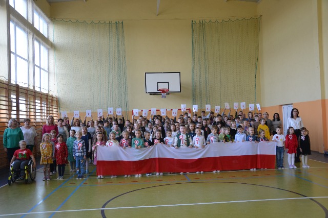 Dzieci na sali gimnastycznej ustawione do zdjęcia z flagą Polski.
