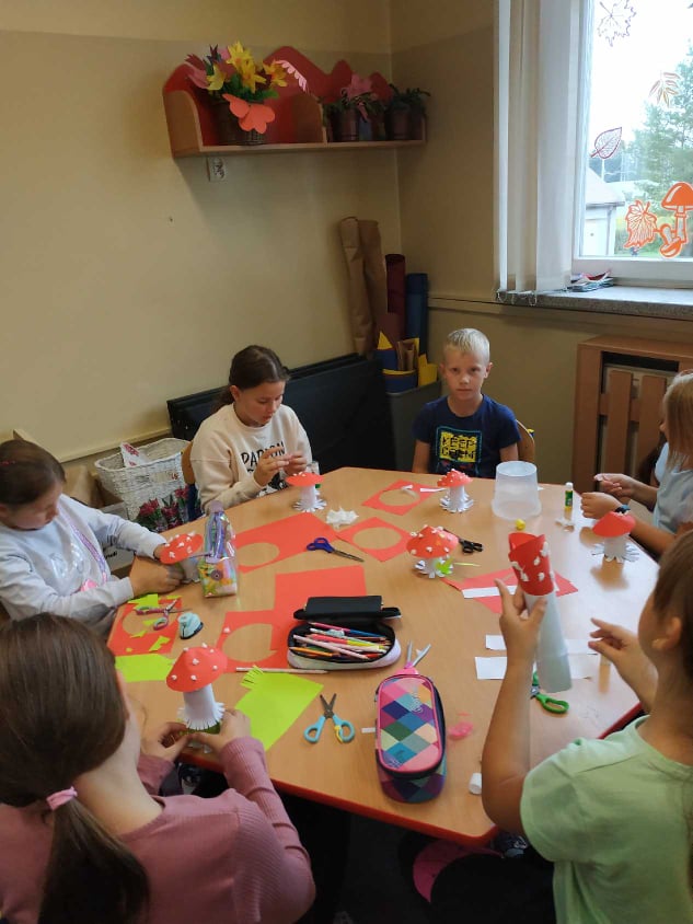 Dzieci siedzą przy stoliku na którym leżą ścinki papieru kolorowego.